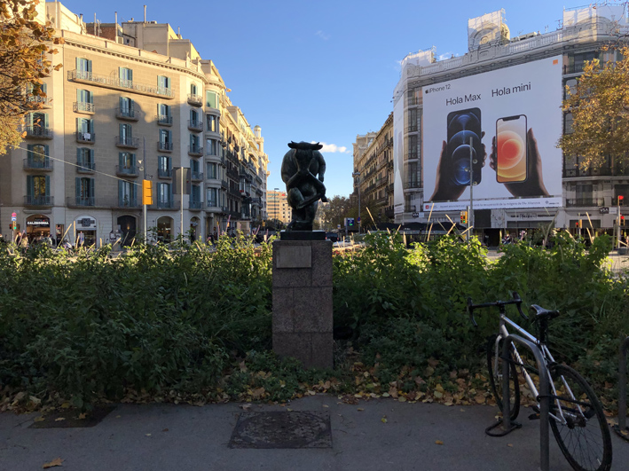 Meditació, the thinking bull statue with buildings behind it and weeds growing around it