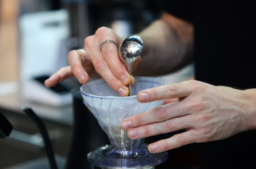Barista's hands stirring coffee in V60 filter funnel