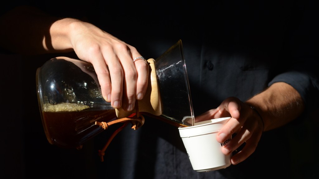 Baristas hands pouring coffee brew from a Chemex coffee maker into a cup